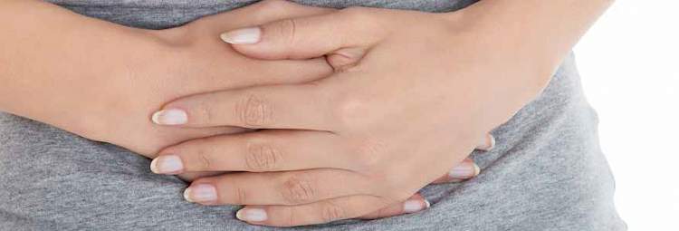 Une femme, avec un T-shirt gris, croise les mains sur son ventre