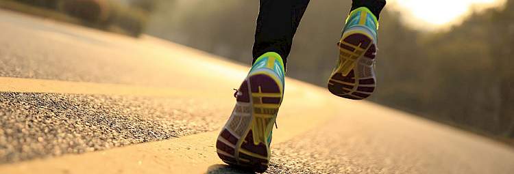 Un homme court en baskets de sport sur une route avec un coucher de soleil